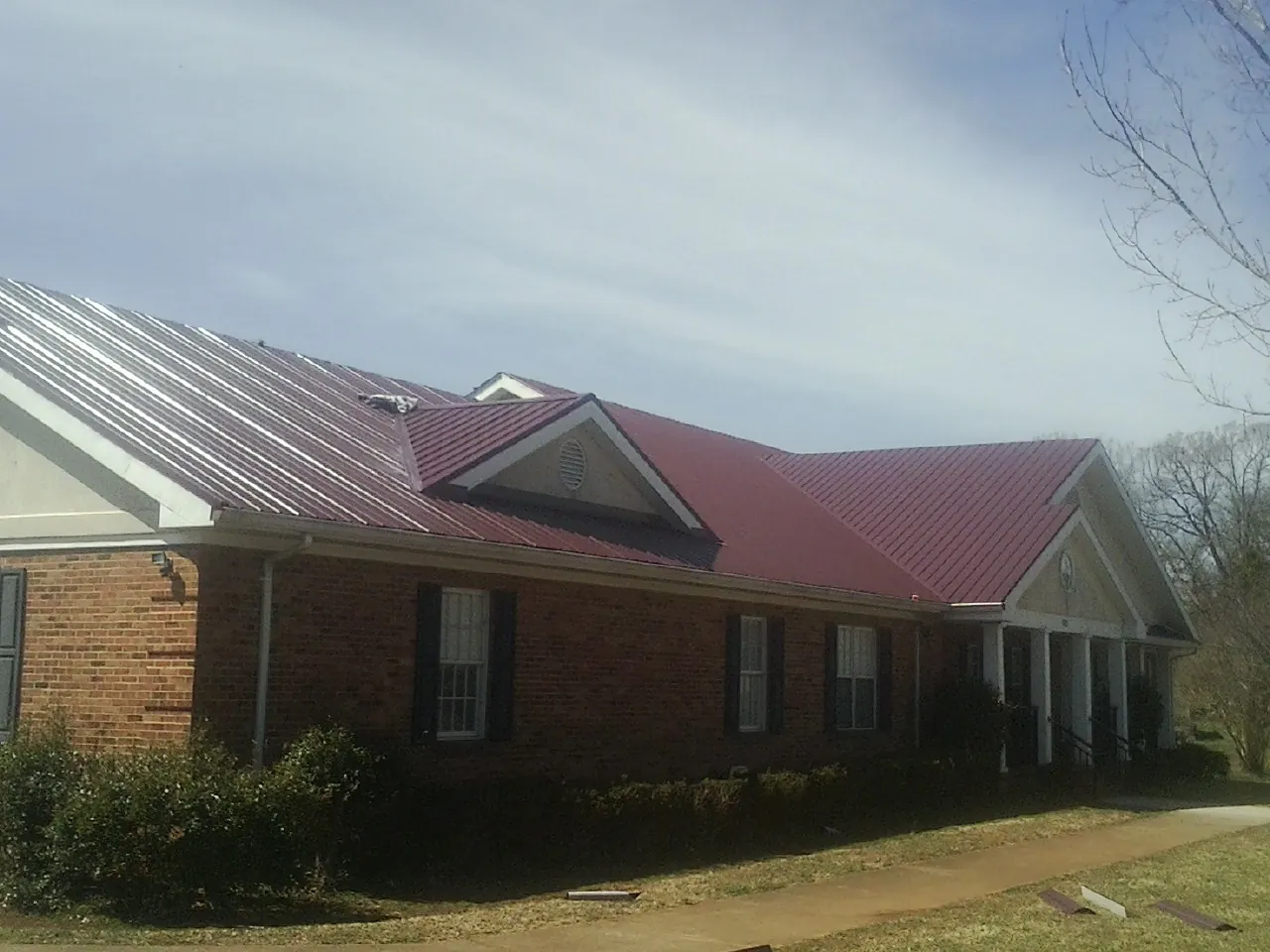 Red metal roof with gabled entries on a long brick building, from a Hail Damage Roof Repair job in Clarence